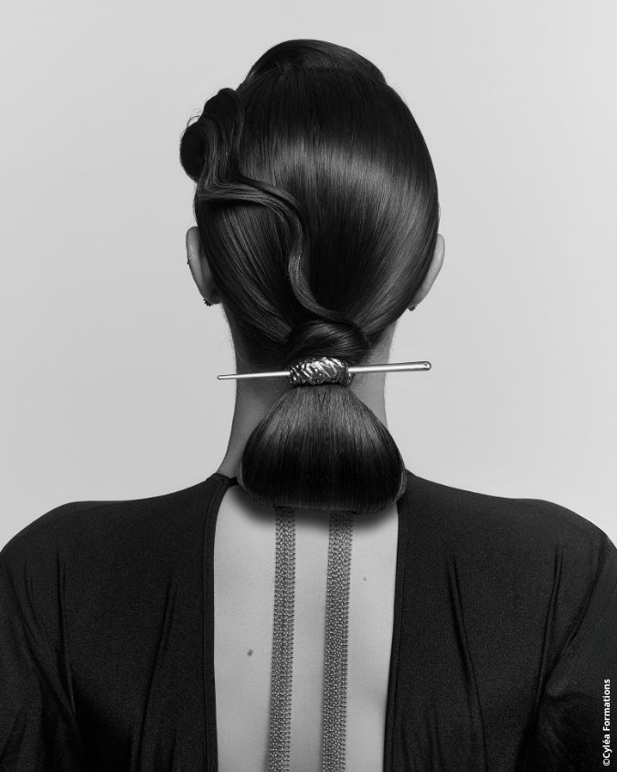 Coiffure artistique et structurée vue de dos, attachée avec un accessoire métallique, photo en noir et blanc pour Cyléa Formations.